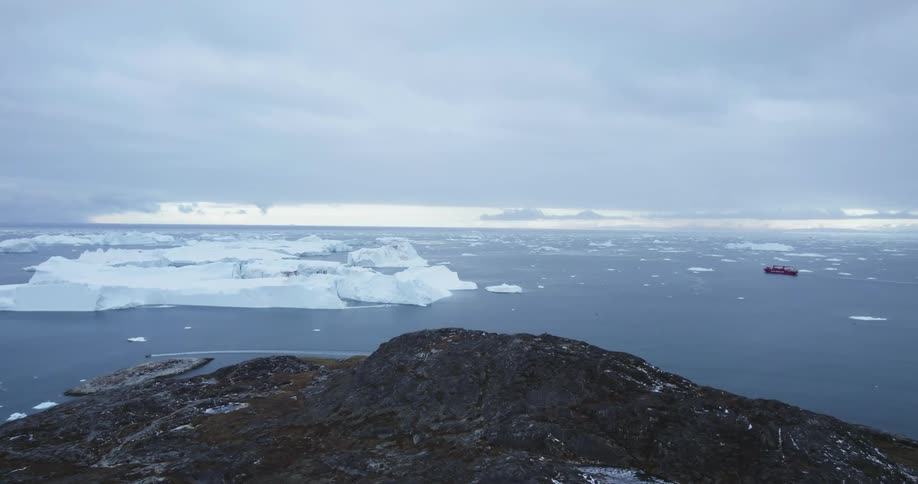 Ship floats among sea ice a distance from shore as smaller moving boat leaves wake