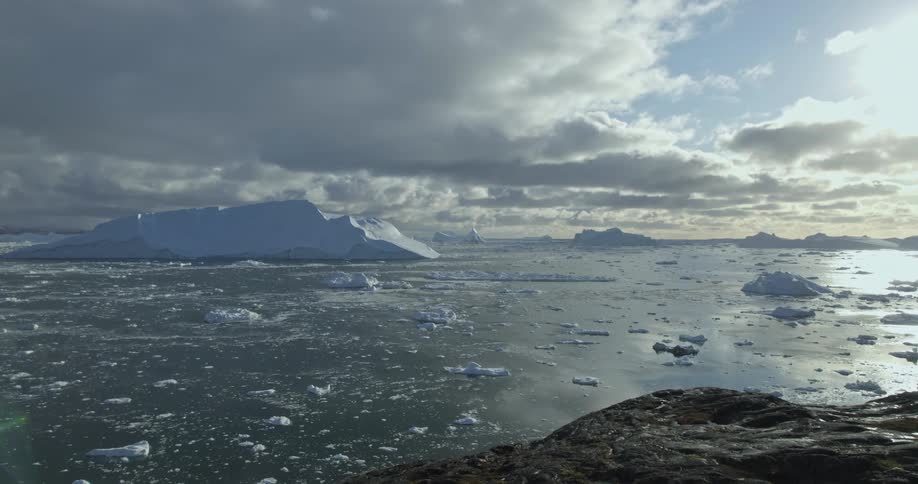 An aerial of ocean waters with ice and glaciers in the ocean and on the landscape