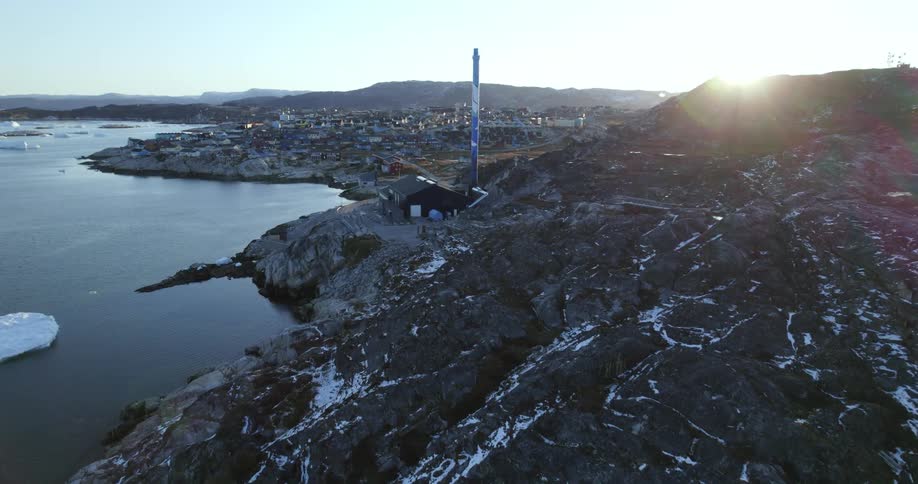Aerial view coming up the coast of greenland with some growlers and the sun rising behind the hill