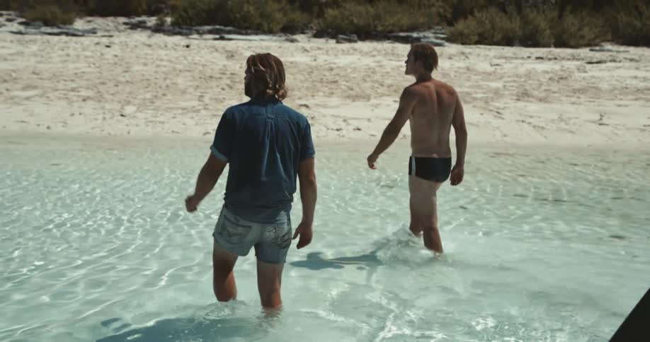Two men walking in the ocean onto a sandy beach