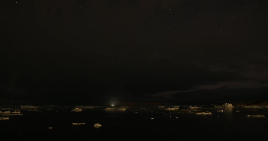 Time lapse of the bright lights on ships sailing around the chunks of ice floating on the arctic sea at night