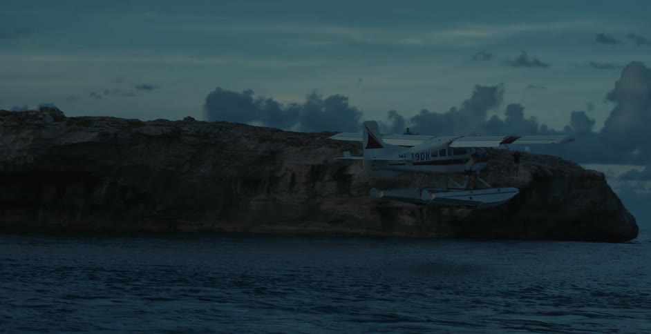 A small private jet flies over the ocean slowly past some large rocks