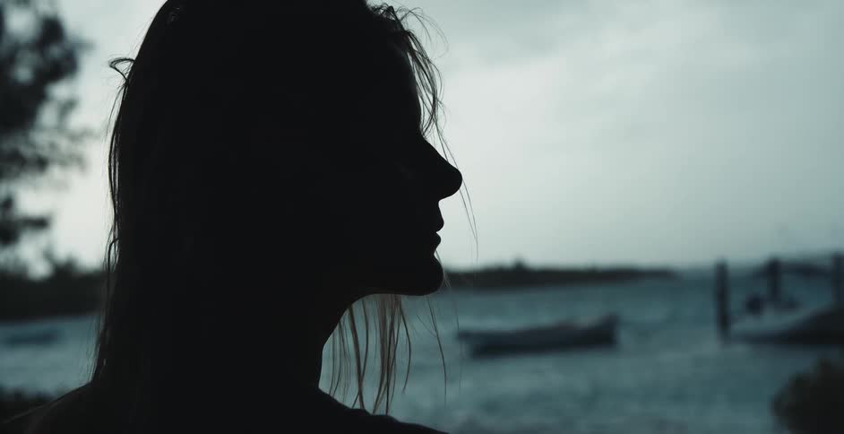 A womans silhouette as she looks out over the water with boats in it