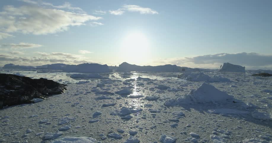 An aerial of icebergs in water with large glaciers and a rock formation meeting the water
