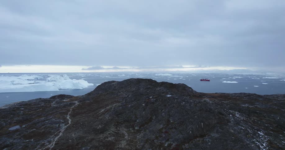 Freighter floats among sea ice a distance from both an icebergand the coast