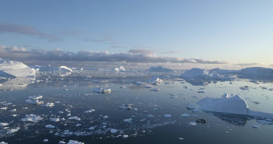 An aerial of icebergs and glaciers in the ocean as a small boat travels through the water
