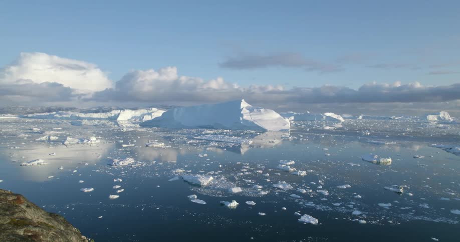 Clouds reflect on the water as icebergs float among pieces melting ice
