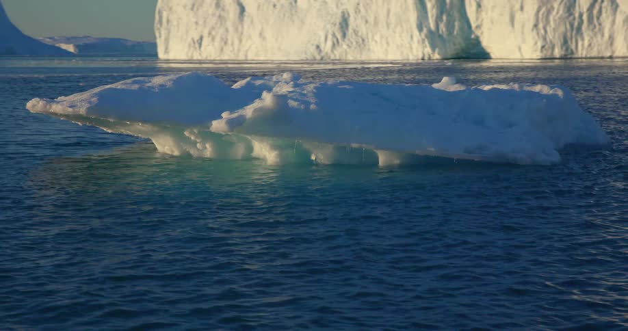 Icebergs in the ocean are displayed at midday