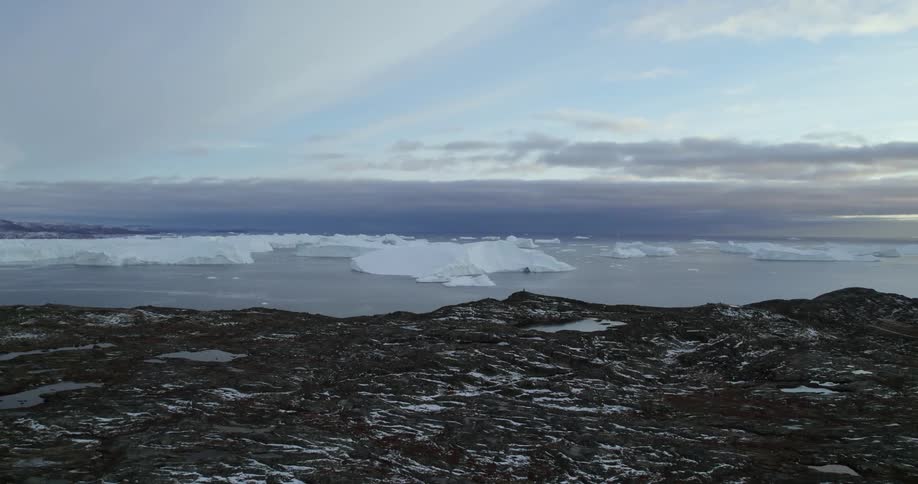 Orbiting aerial view of icebergs floating in the arctic ocean near the coast at morning