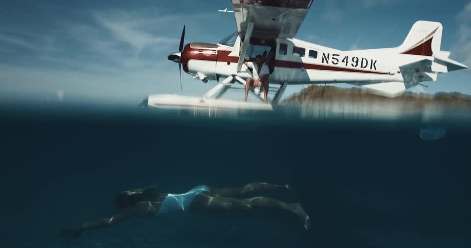 Woman swims underwater near seaplane where man sits
