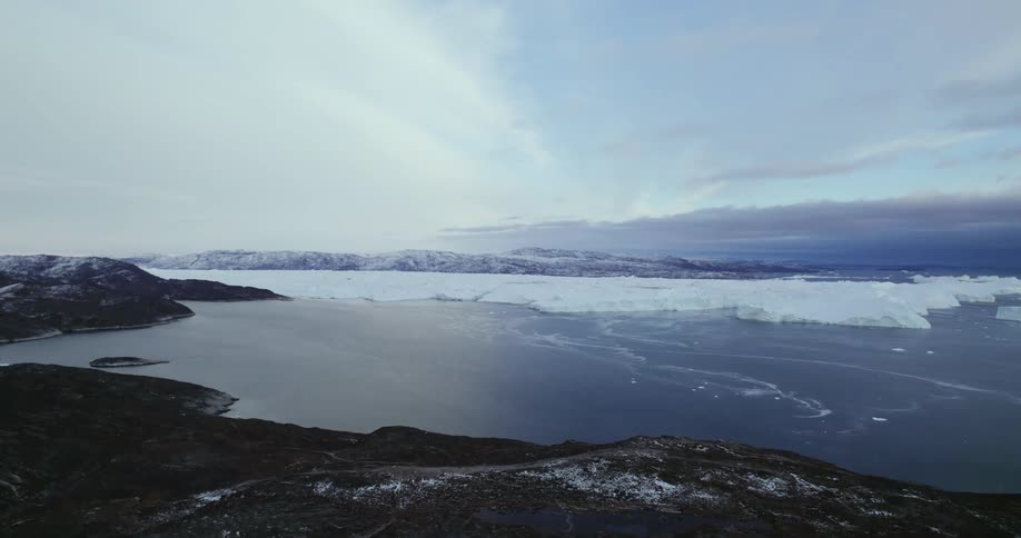 Scattered ice covers coast across ocean from ice sheet on a cloudy day