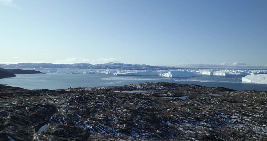 An aerial of coastal mountains in the arctic ocean with icebergs and glacial ice covering the landscape