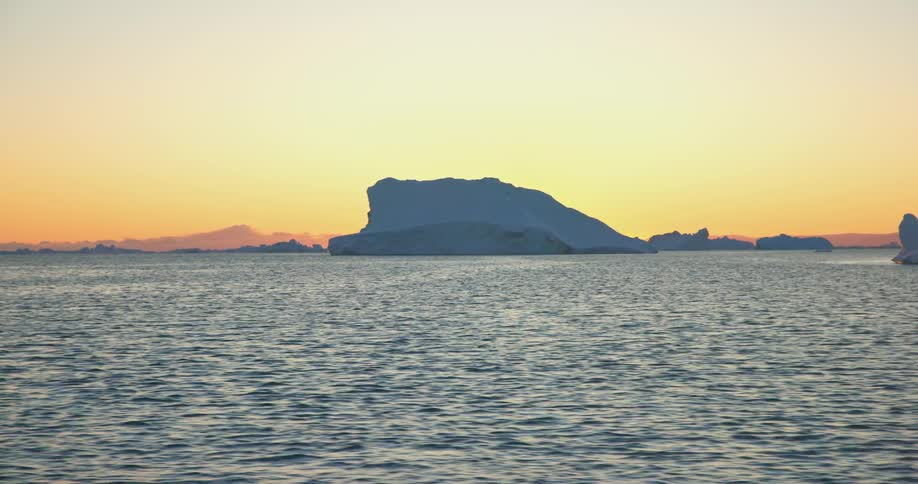 Large icebergs in the ocean with a yellow sunset on the horizon