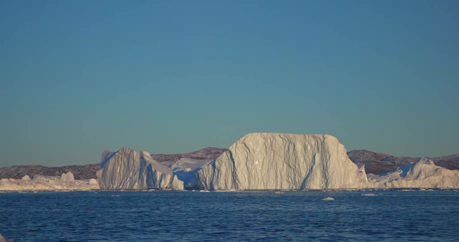 The sun shines brightly upon glaciers as melting ice floats across the water