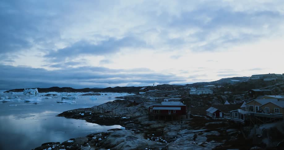 A time lapse of a rural village on the edge of icy waters as it turns from dawn to day