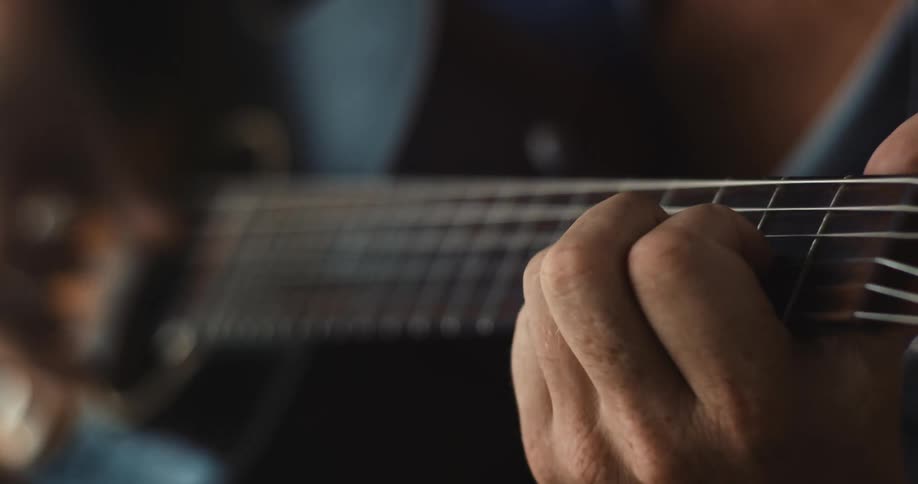 A musician is moving their fingers across the strings on the fretboard as they play an acoustic guitar