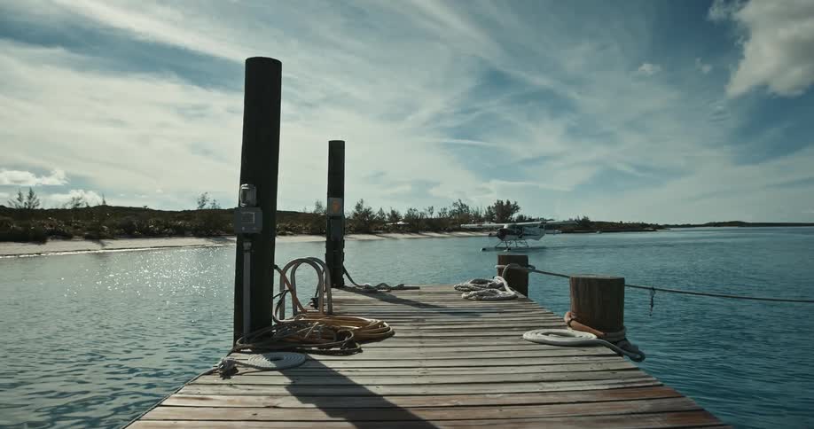 Seaplane coasts through water toward pier on cloudy day