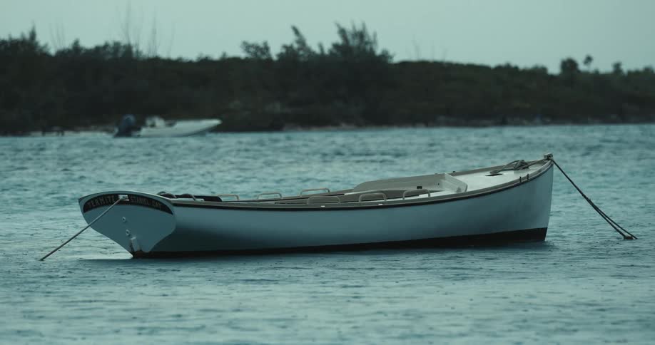 A boat anchored in water as it rains and another boat is anchored near trees
