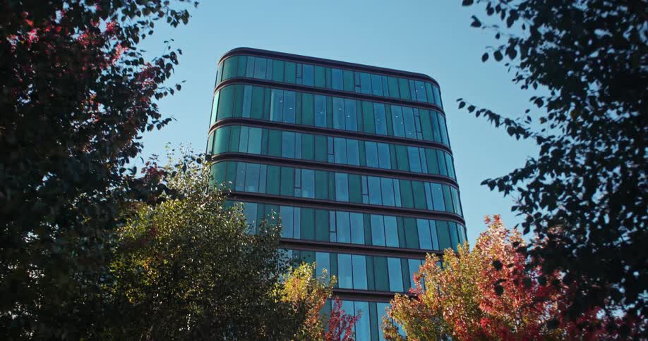 A tall building with windows on all side with colorful trees lined up below it