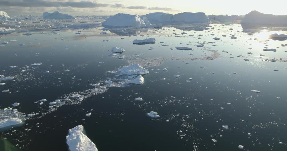 Clouds and sunlight reflect on the water as icebergs float among pieces melting ice