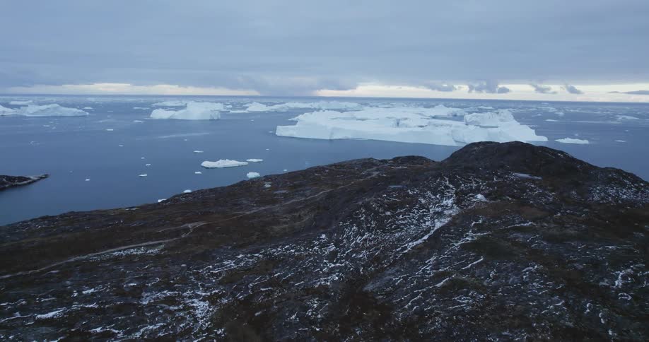 An aerial of a mountain coastline in the arctic ocean with icebergs in the water