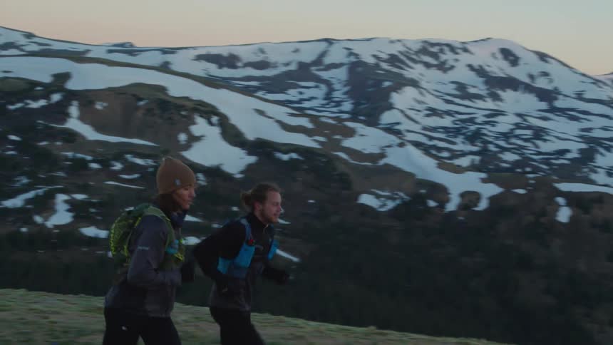 Young men wearing sports clothes jogging on the slopes of a snow covered mountain range at evening