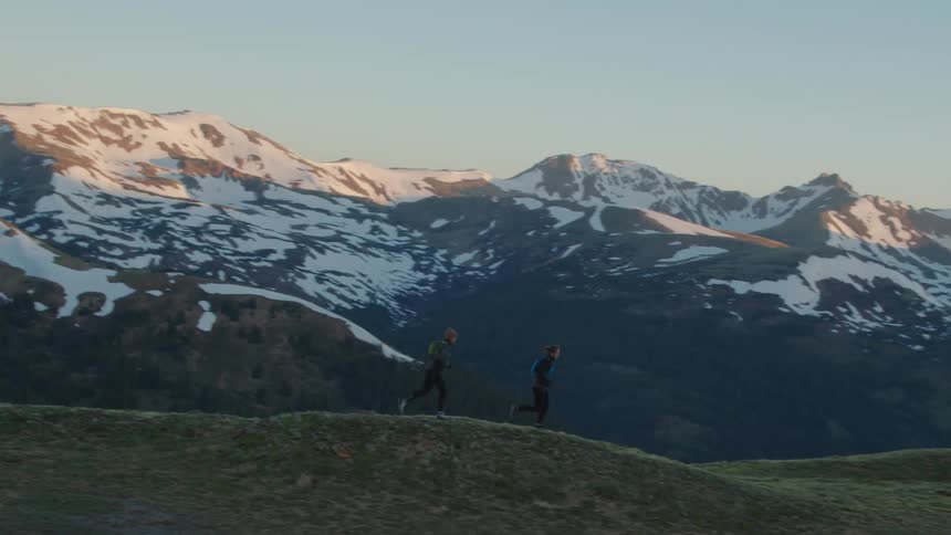 Pair of runners run across hills with snowy mountains in the background