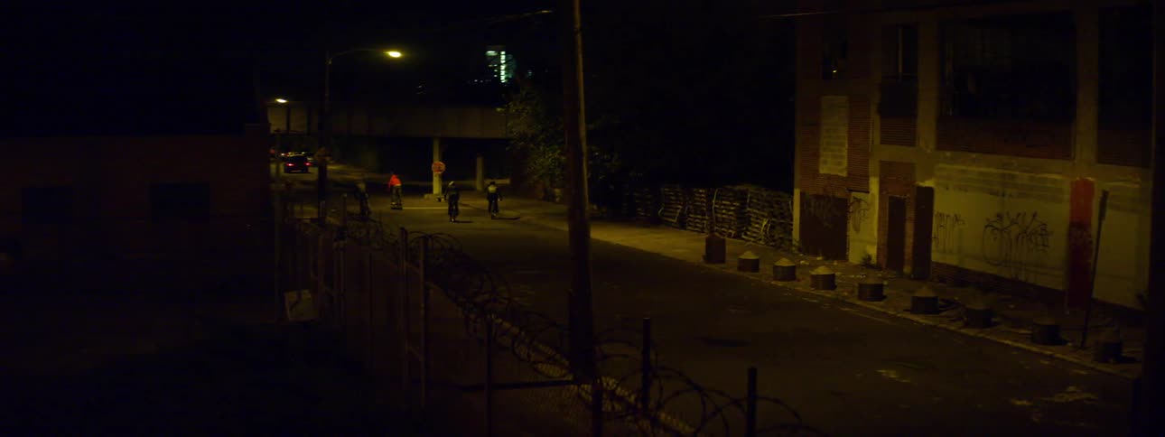People riding their bikes down a run down city street at night