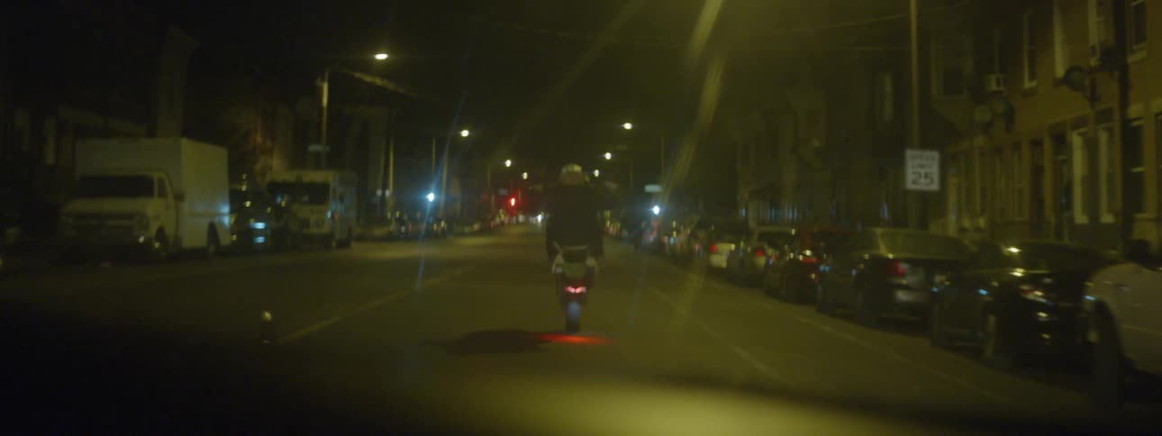 A small motorcycle rides down the middle of a city street with a car following
