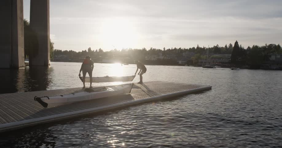 Two people lift kayaks into the water off a dock