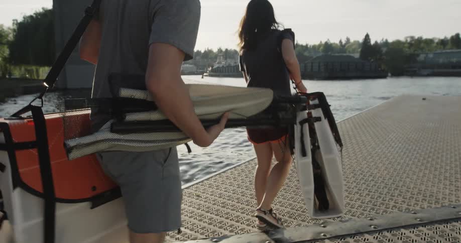 A man and woman carry equipment by the water