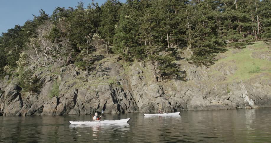 Two people paddling kayaks in a river next to a tall cliff