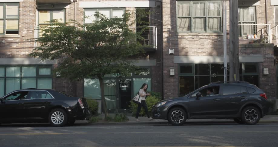 A woman waiting on the sidewalk gets into a car that pulls up