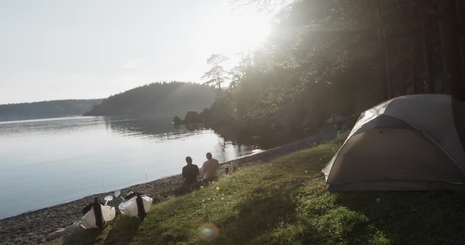 Two people sit down by the water of a lake