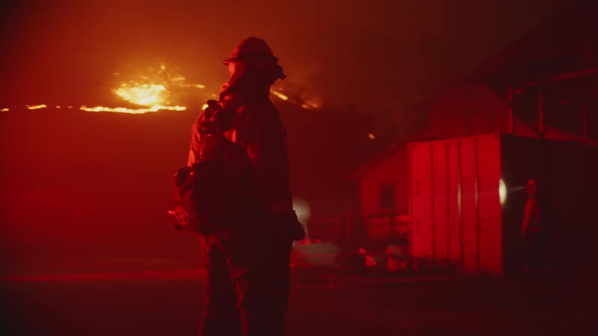 Firefighter stand and walk outside a home as it burns