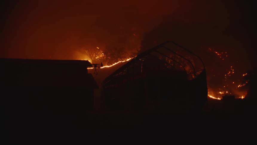 A silhouette of a house and structure with a forest fire burning in the distance