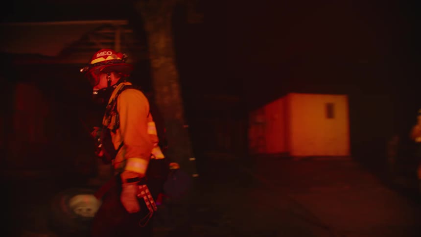 Firefighters surveys the area around a wildfire in the forest at night
