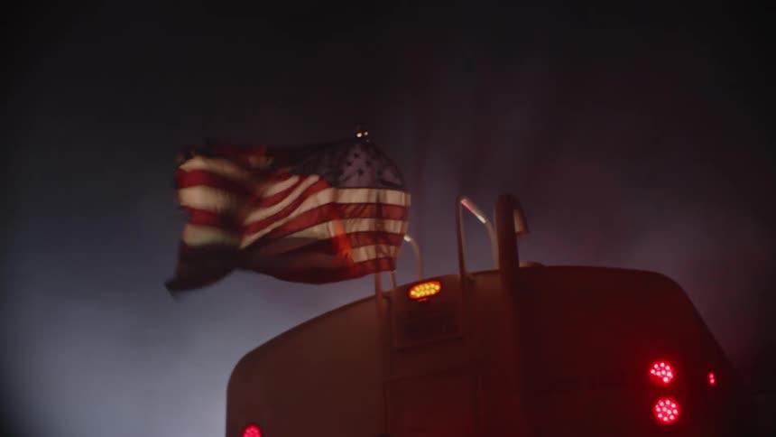 American flag waving in the wind behind a tanker truck driving at night