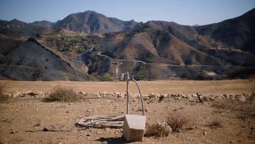 A water faucet in the middle of a field next to the mountains at daytime