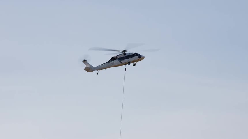 A helicopter flies in the air as a cable hangs down below