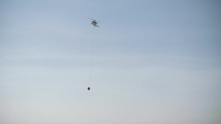 A helicopter carries an object attached to a rope ladder over mountains