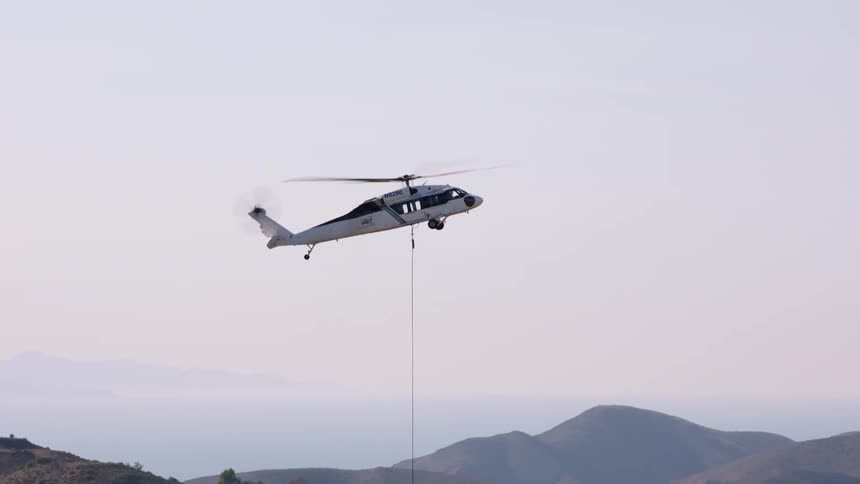 A red bucket being lowered on a cable attached to a helicopter hovering in the air