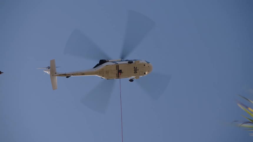 The bottom side of a helicopter as it hovers in one place with a cable hanging down