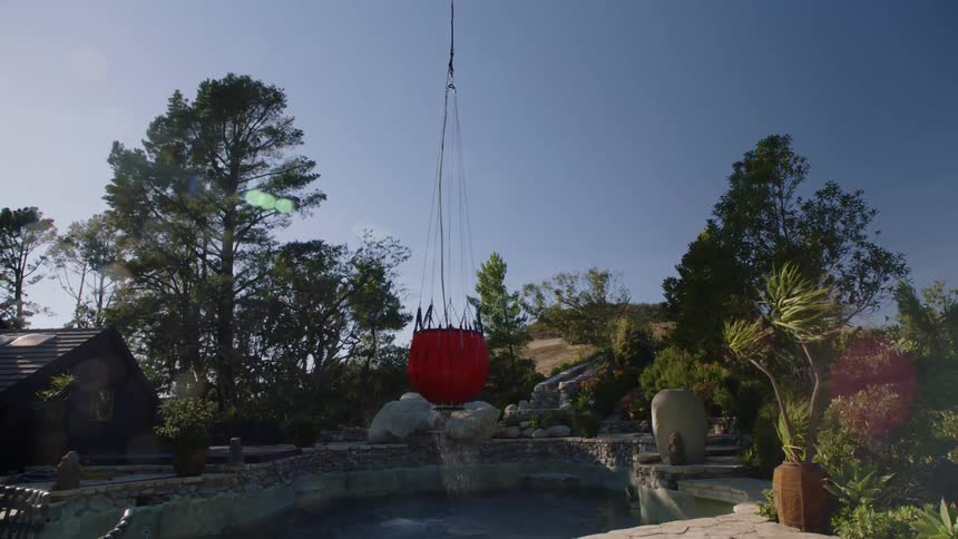 A helicopter lifts a red object out of a swimming pool at a home