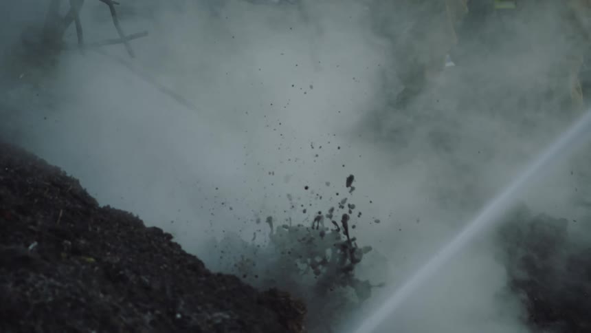 Water sprayed onto smoking ground churns dirt creating mud