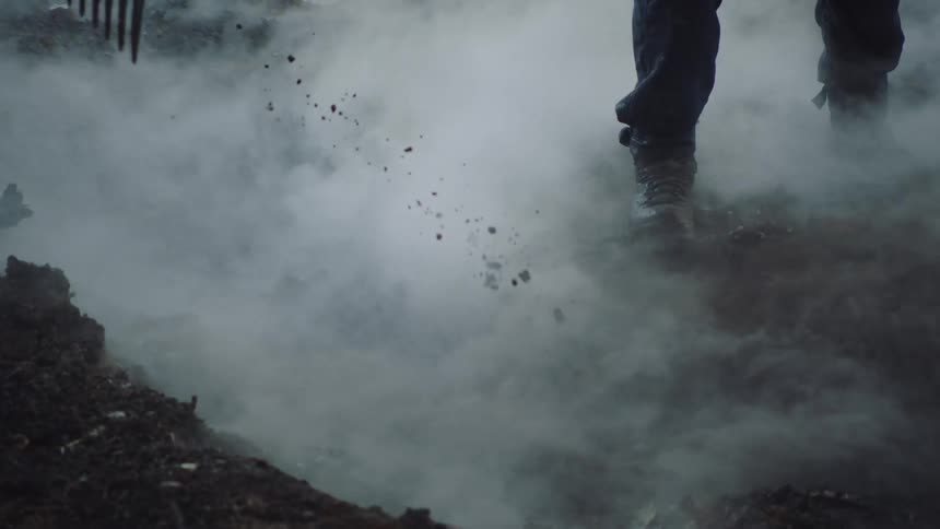 Firefighter rakes smoking ground as water is sprayed onto same area