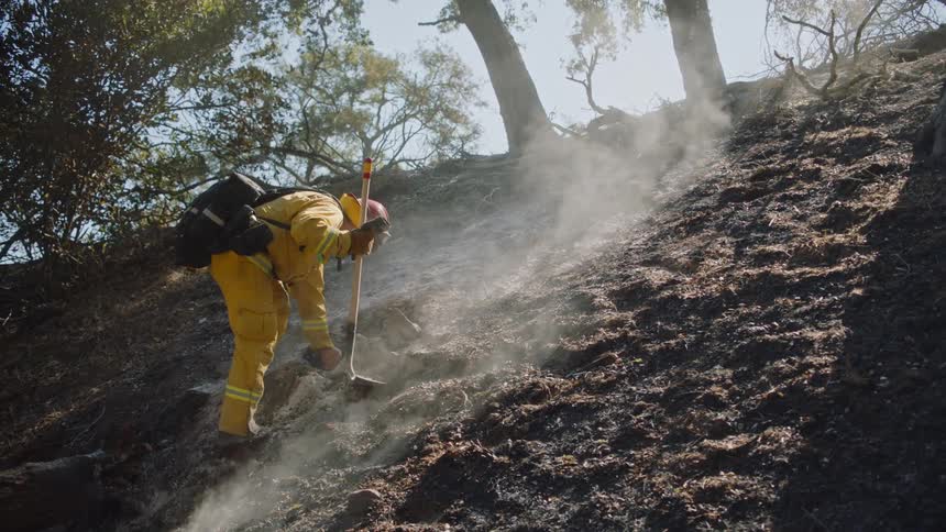 A firefighter tests the heat level in the ground following a forest fire
