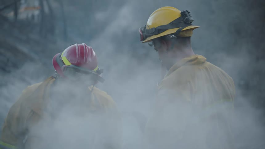 Smoke surrounds two firefighters as they examine an area by a mountain