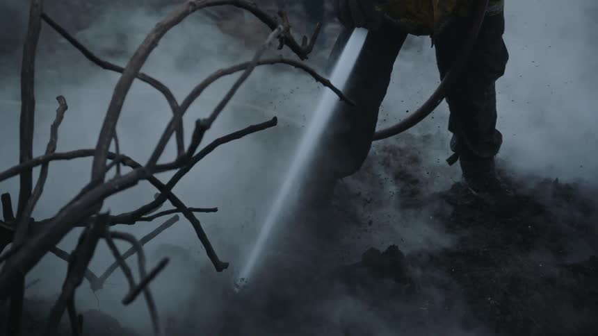 Firefighter sprays water onto smoking ground