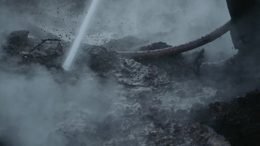 Firefighter sprays steaming charred ground with water creating mud